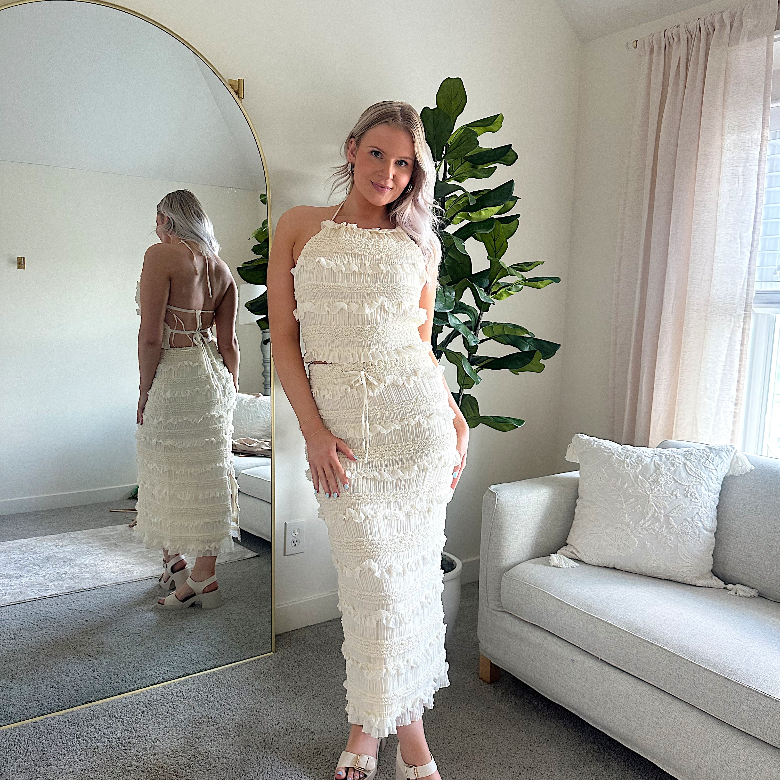 Woman wearing ivory two piece set with halter tie back top and smocked ruffled midi skirt