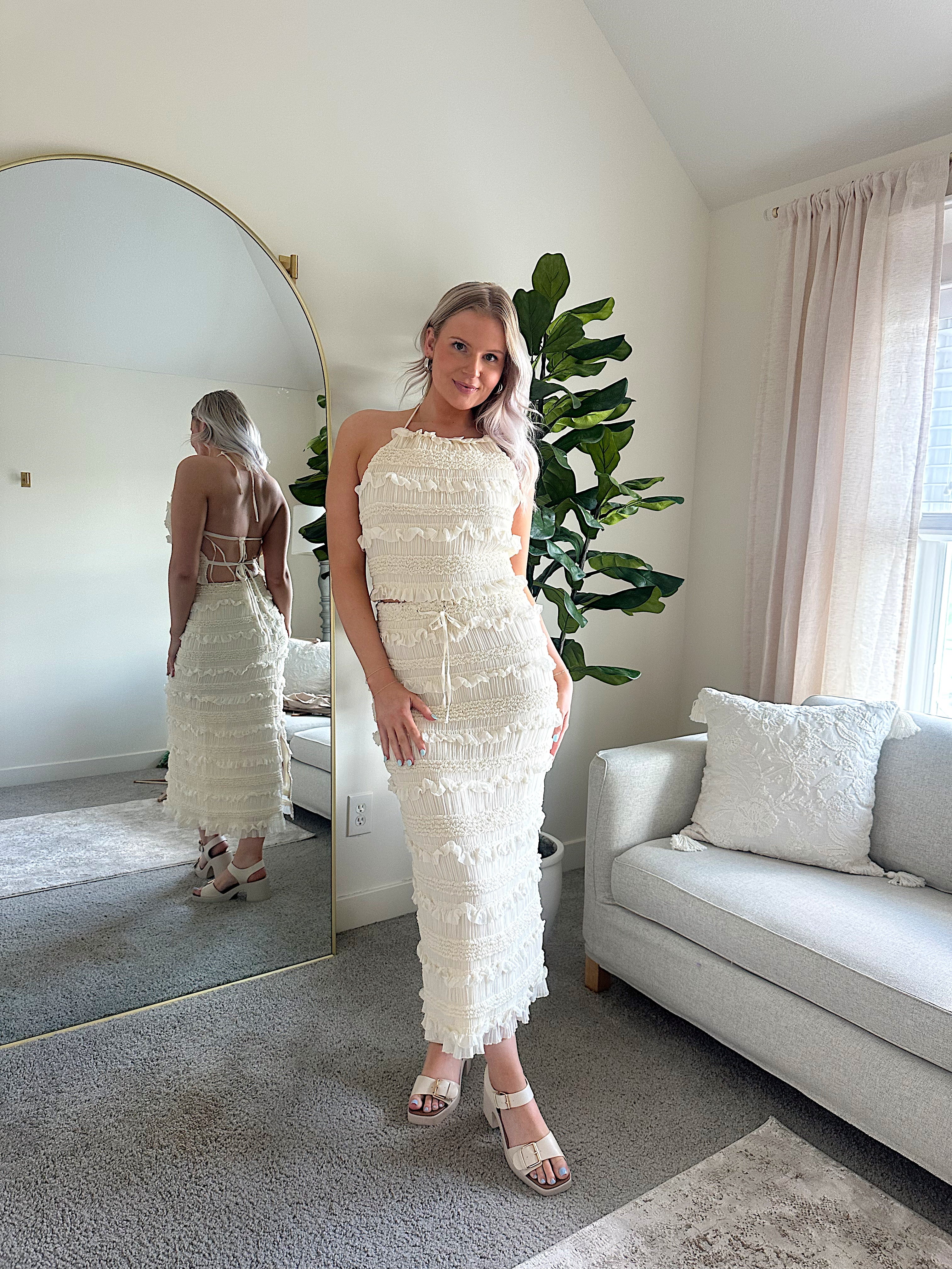 Woman wearing ivory two piece set with halter tie back top and smocked ruffled midi skirt