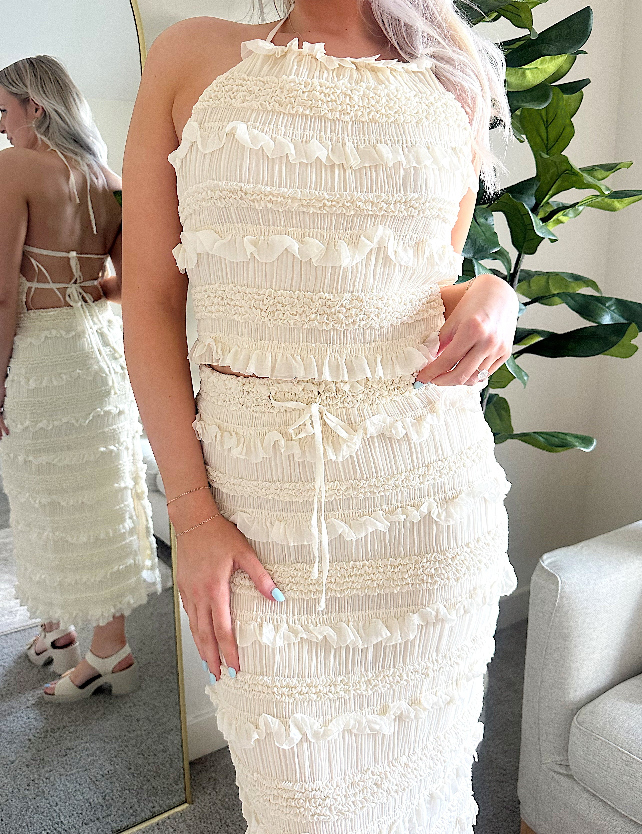 Woman wearing ivory two piece set with halter tie back top and smocked ruffled midi skirt