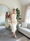 Woman wearing ivory two piece set with halter tie back top and smocked ruffled midi skirt