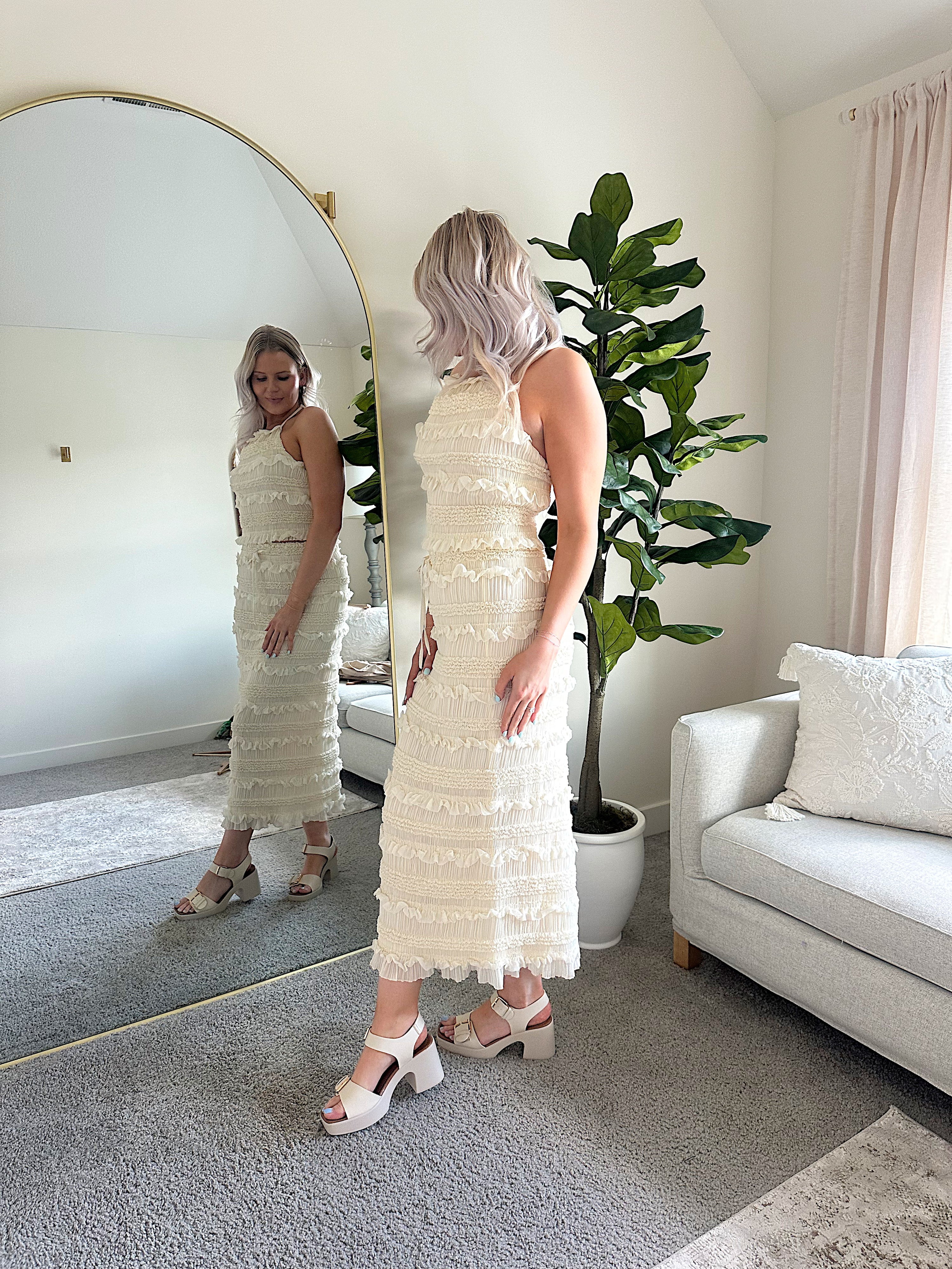 Woman wearing ivory two piece set with halter tie back top and smocked ruffled midi skirt