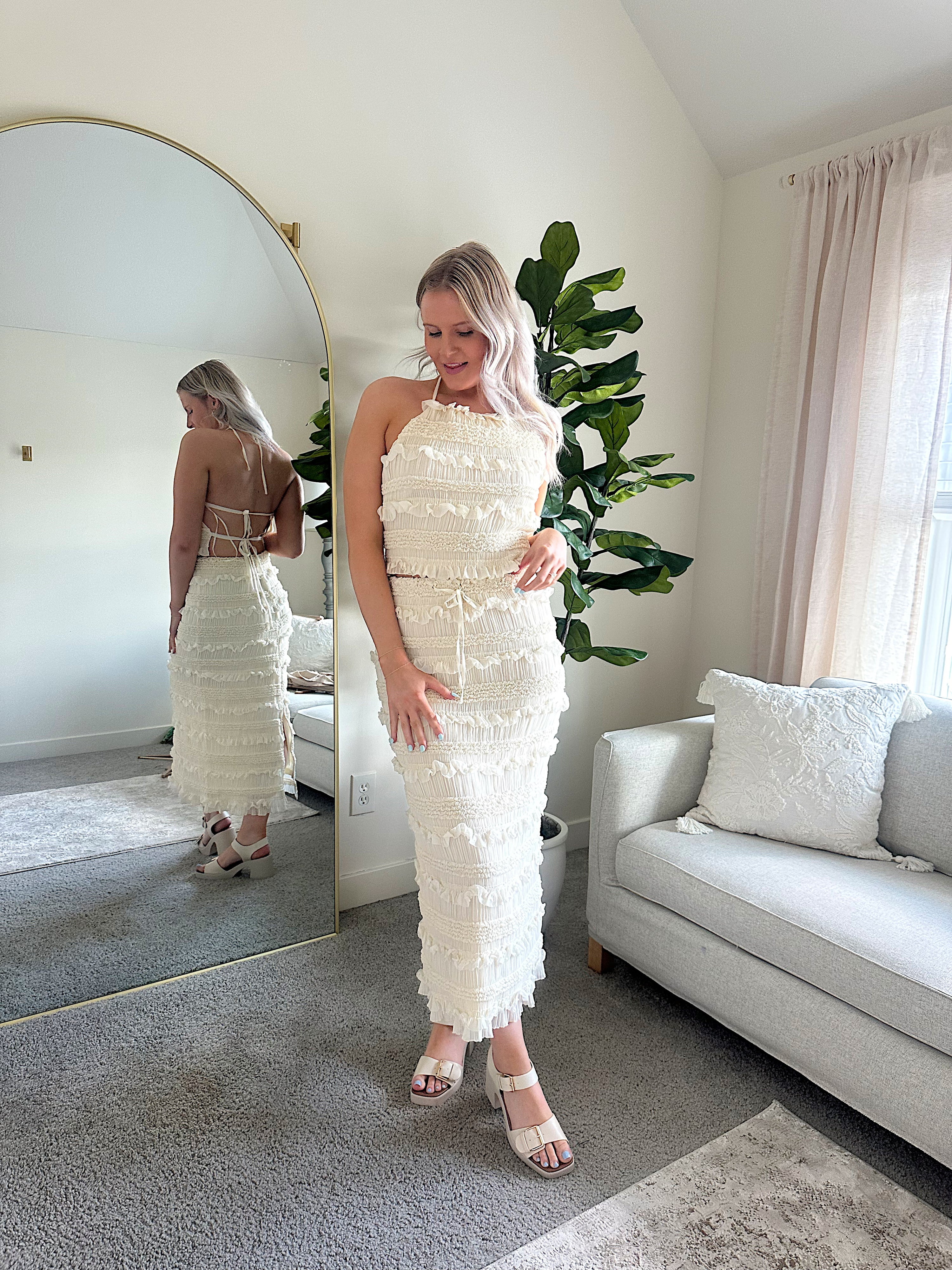 Woman wearing ivory two piece set with halter tie back top and smocked ruffled midi skirt