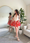 Woman wearing a beige deep V mini dress with a red and white tropical print skirt and fitted waistline.