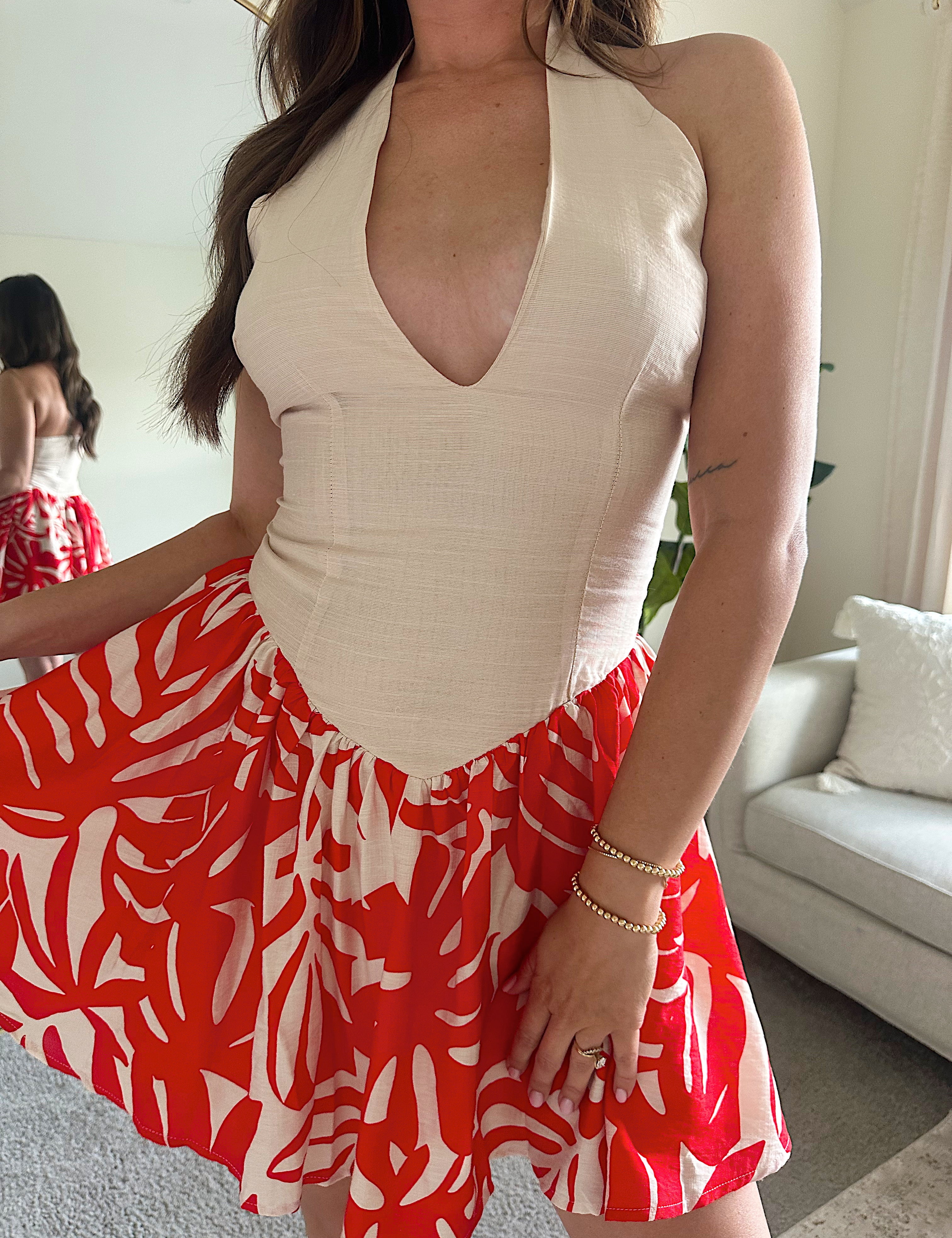 Woman wearing a beige deep V mini dress with a red and white tropical print skirt and fitted waistline.