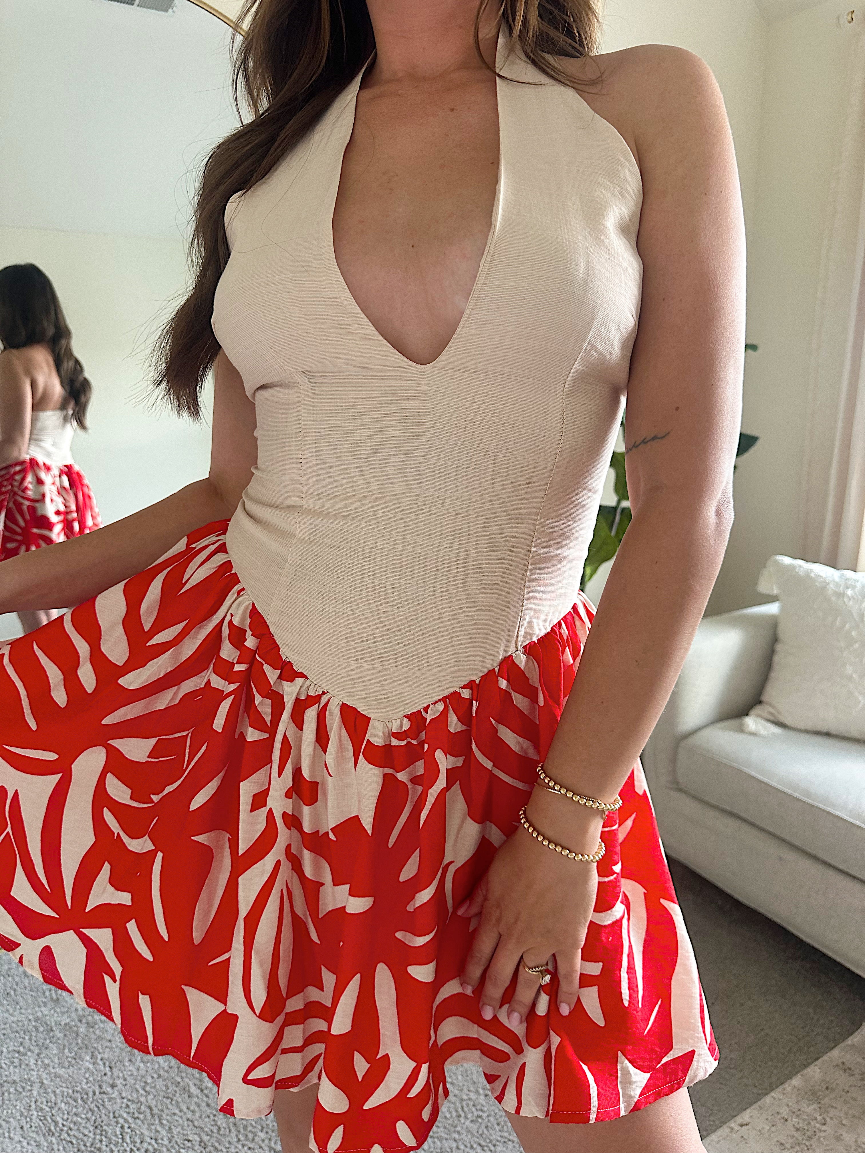 Woman wearing a beige deep V mini dress with a red and white tropical print skirt and fitted waistline.