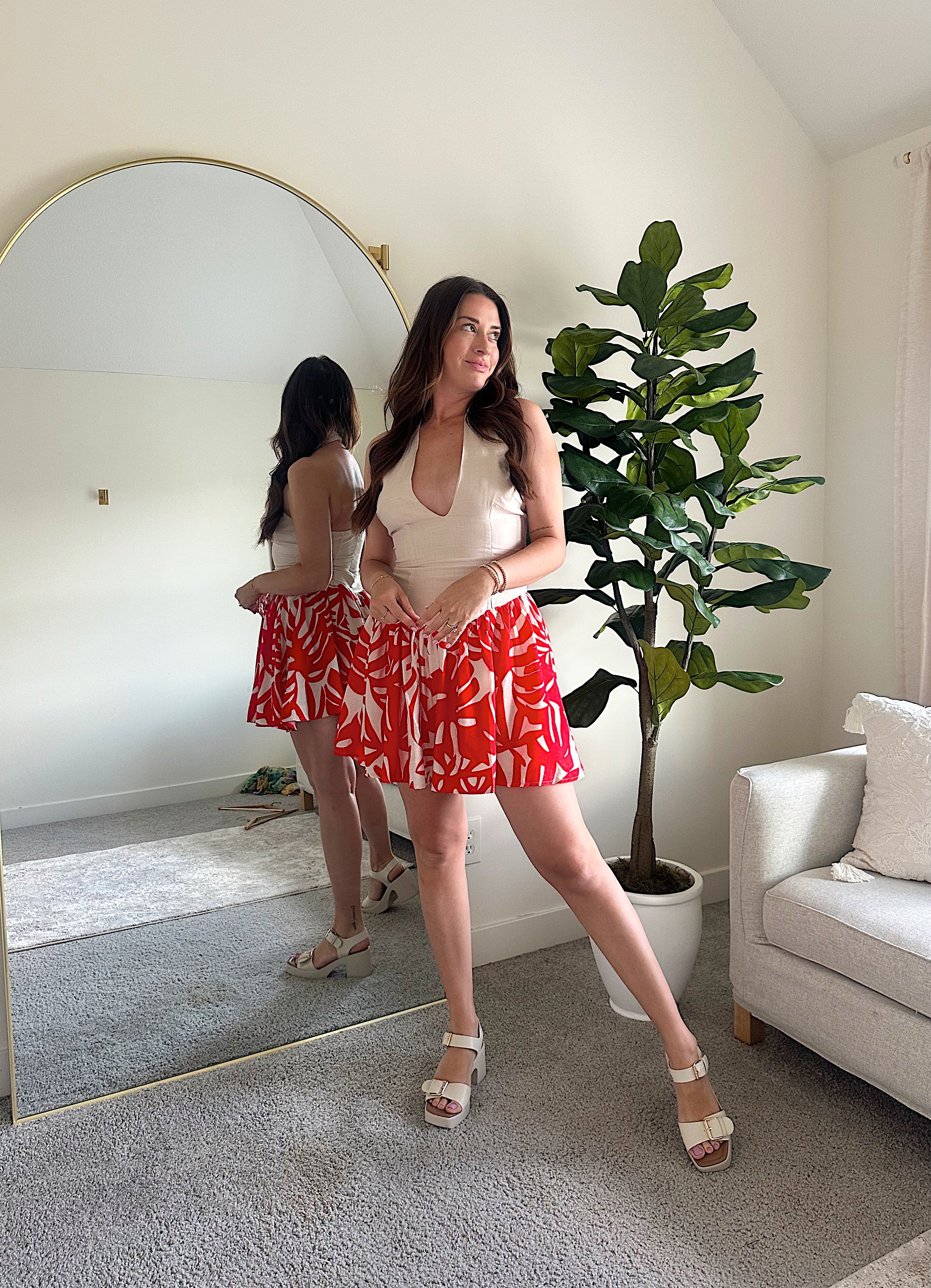 Woman wearing a beige deep V mini dress with a red and white tropical print skirt and fitted waistline.