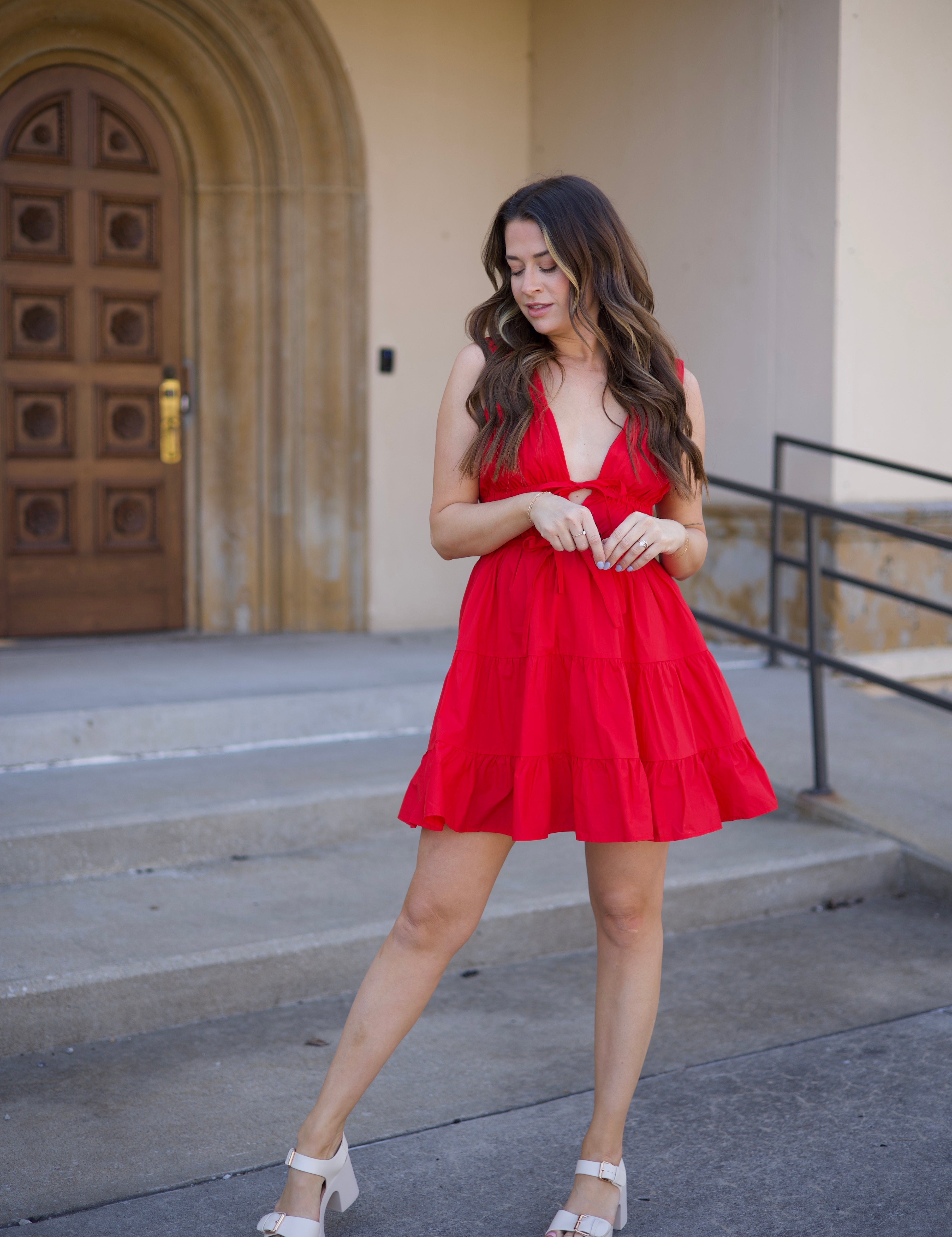 Kerry Tiered Mini Dress in red with a plunging neckline and tiered ruffles, twirling in front of an arched doorway.