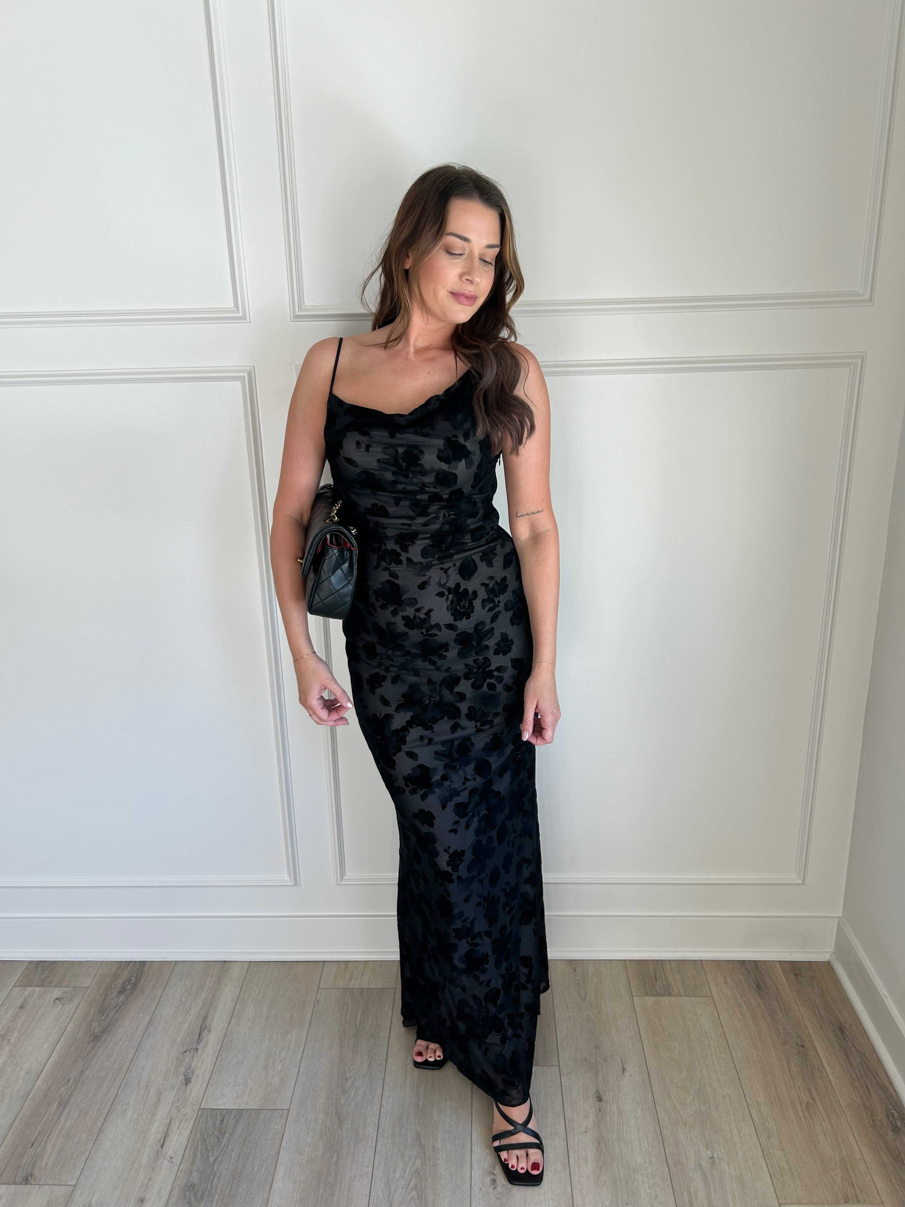 Black floral velvet maxi dress with spaghetti straps, cowl neckline, and sheer detailing for elegance.