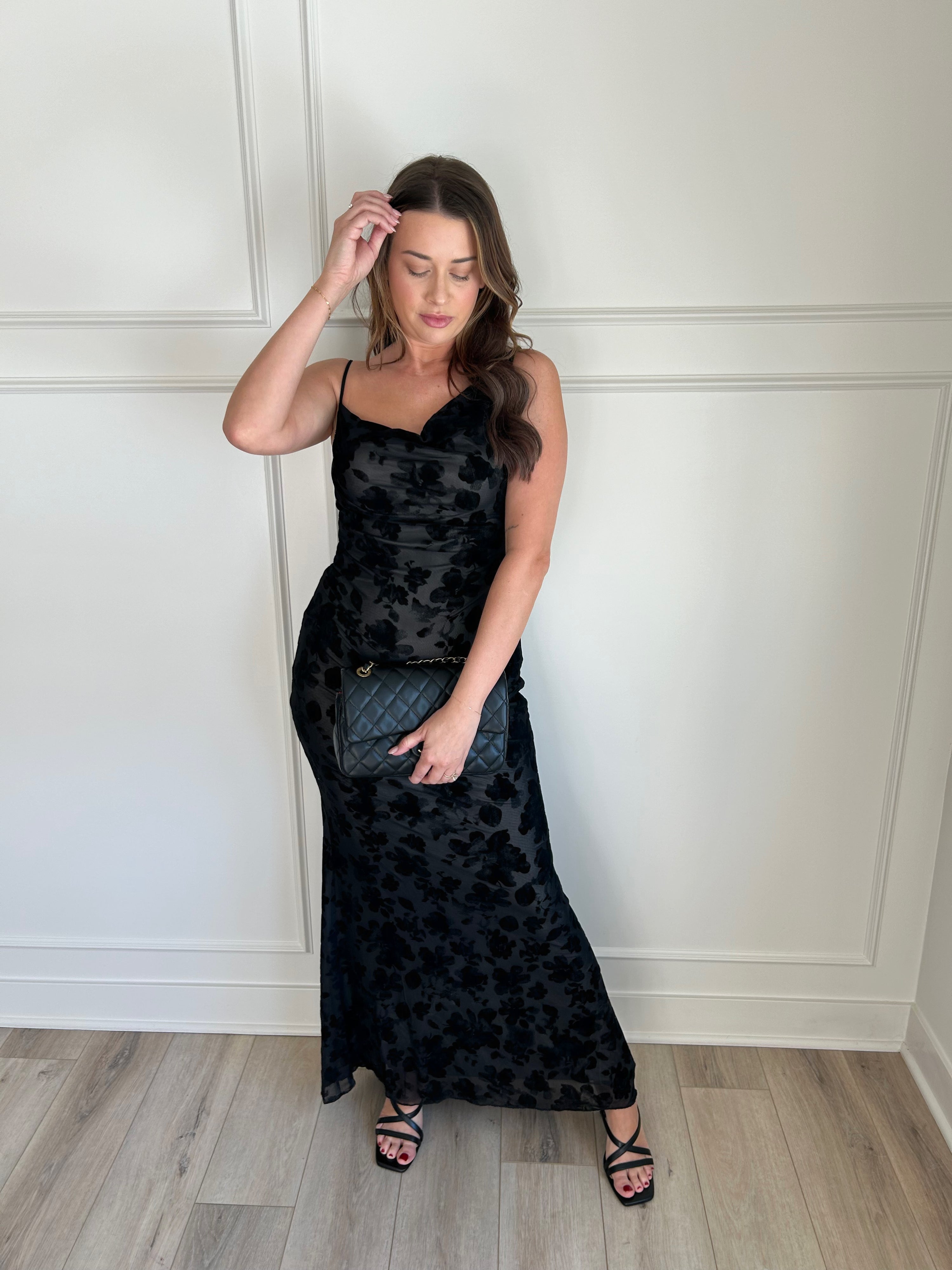 Black floral velvet maxi dress with spaghetti straps, cowl neckline, and sheer detailing for elegance.