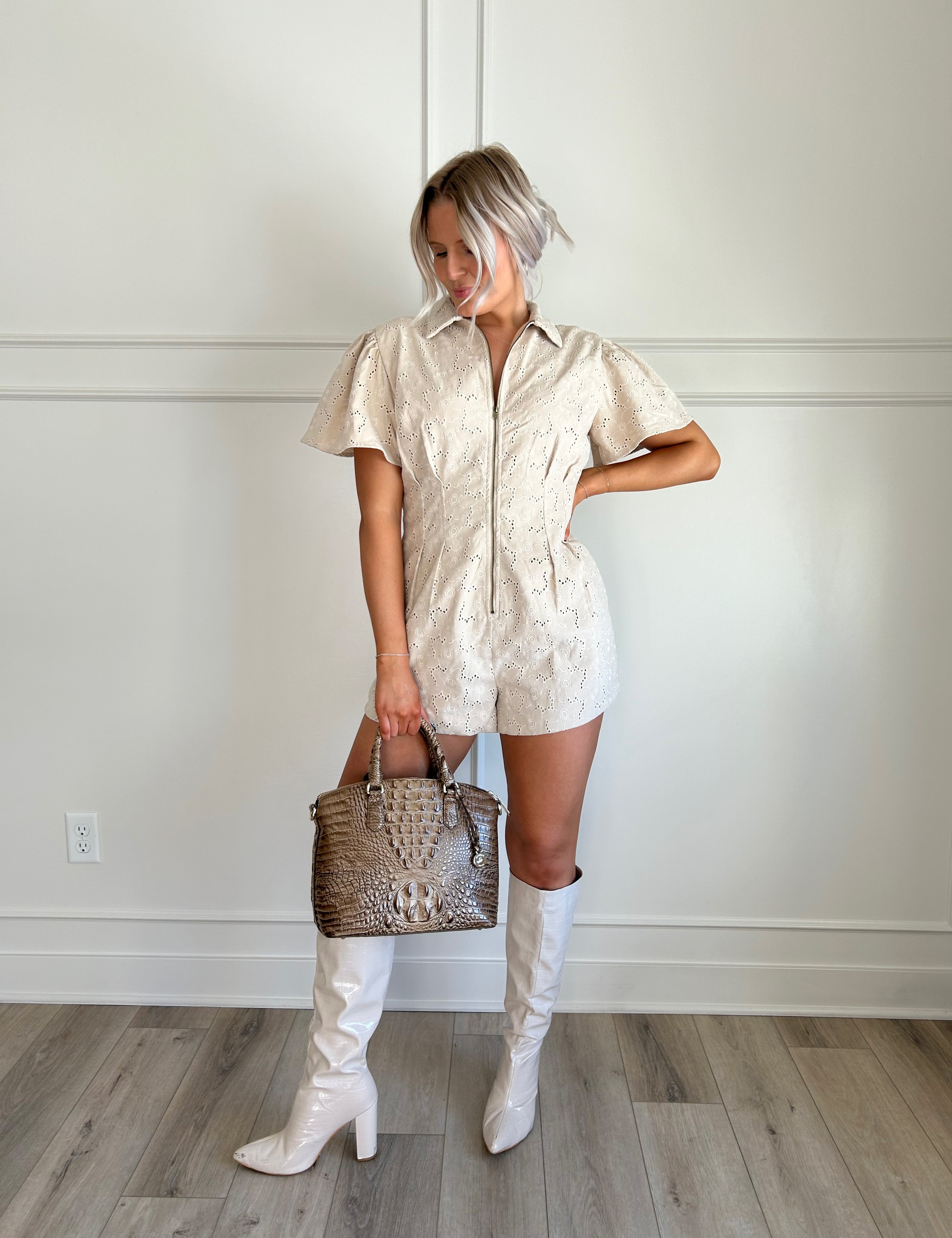 Beige eyelet romper with puff sleeves, zip-front closure, and functional pockets for stylish convenience.