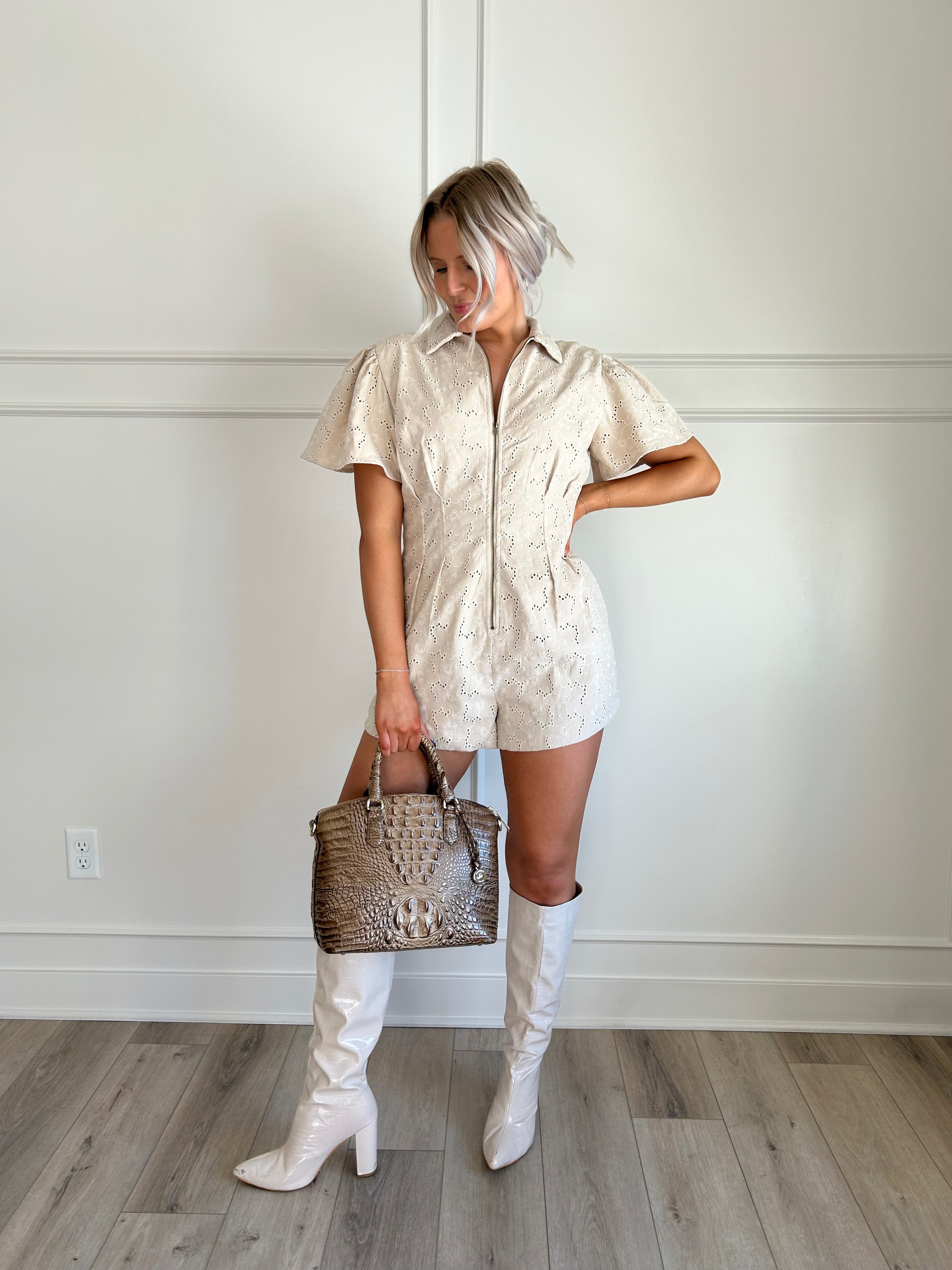 Beige eyelet romper with puff sleeves, zip-front closure, and functional pockets for stylish convenience.