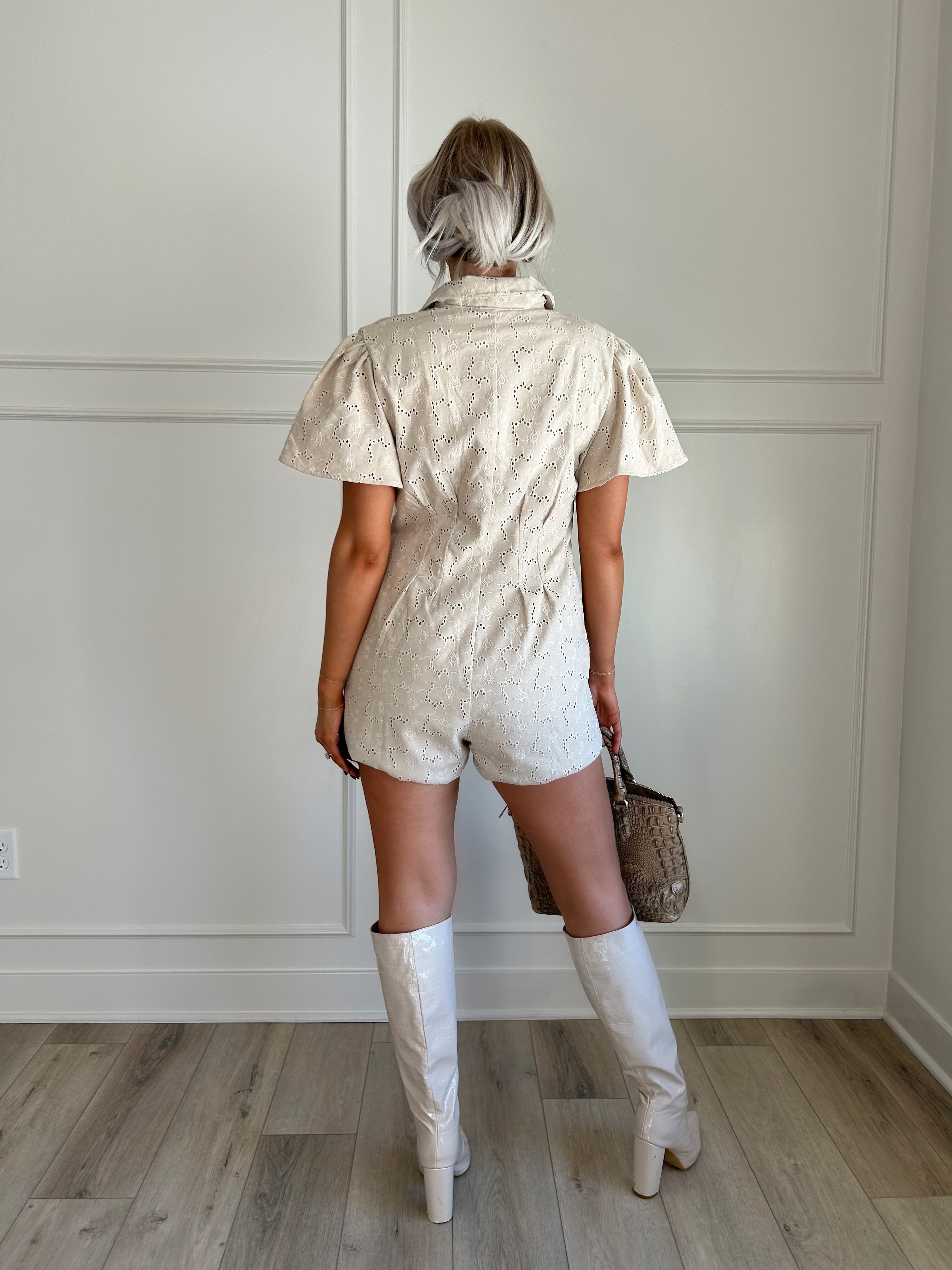 Beige eyelet romper with puff sleeves, zip-front closure, and functional pockets for stylish convenience.