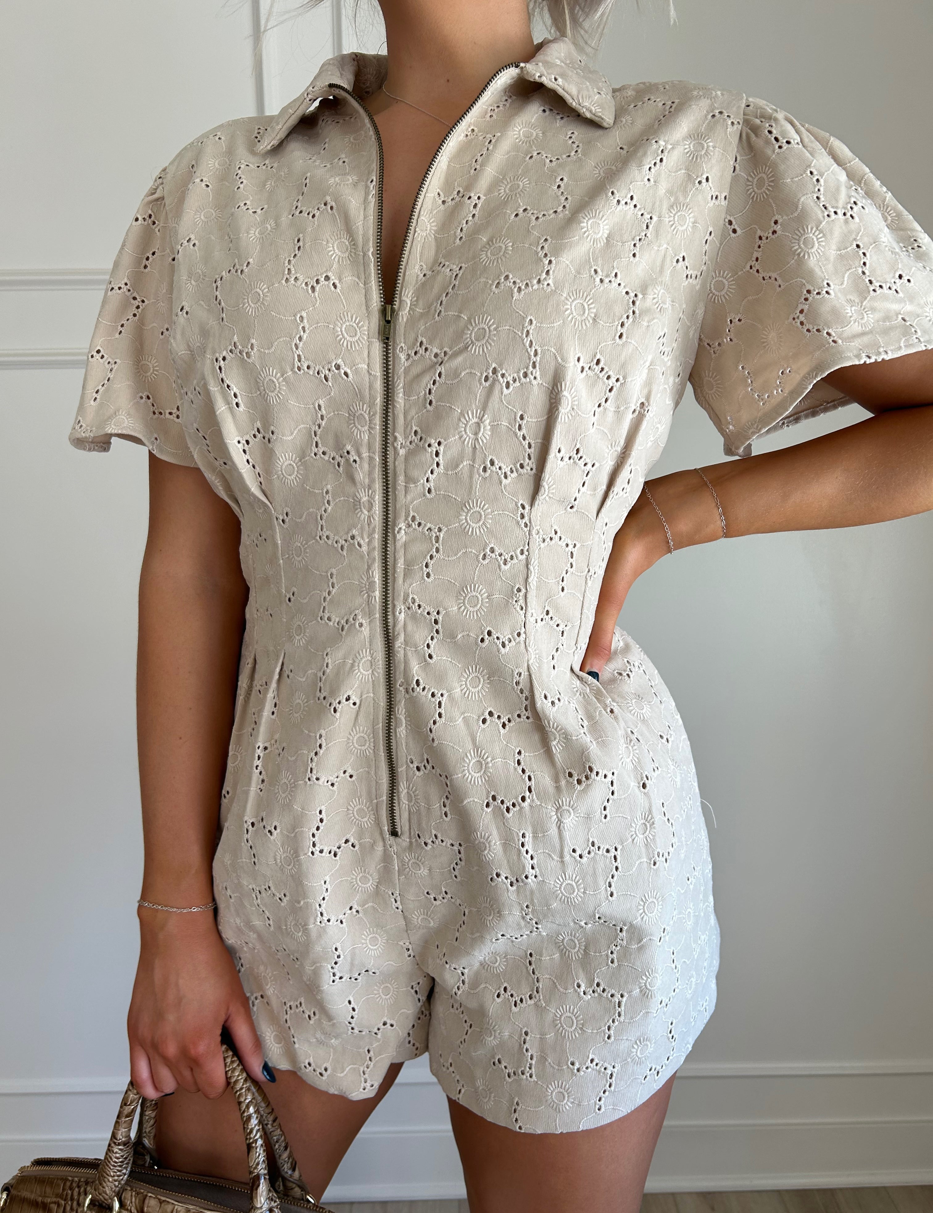 Beige eyelet romper with puff sleeves, zip-front closure, and functional pockets for stylish convenience.