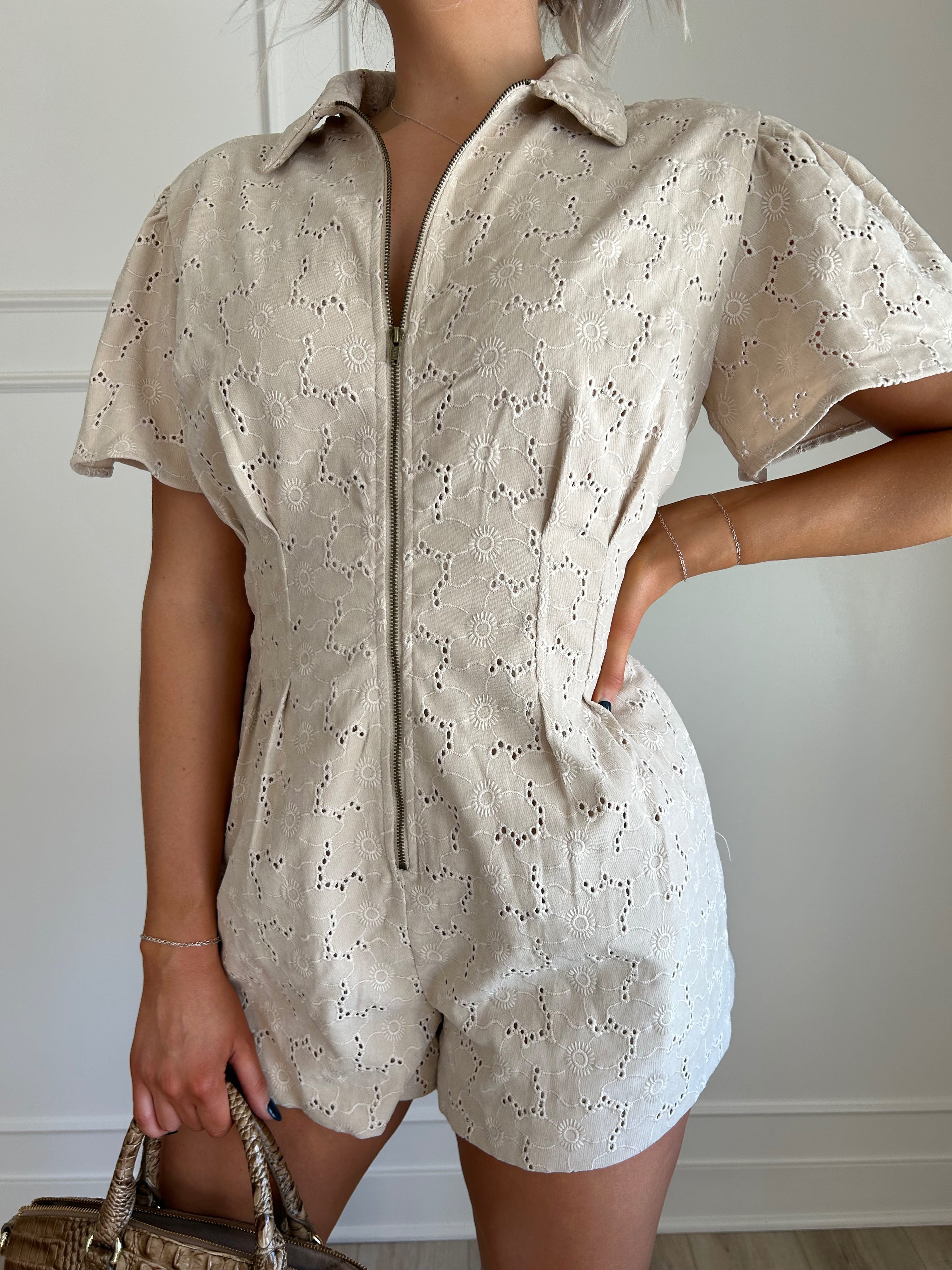 Beige eyelet romper with puff sleeves, zip-front closure, and functional pockets for stylish convenience.