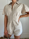 Beige eyelet romper with puff sleeves, zip-front closure, and functional pockets for stylish convenience.