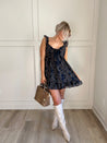 Navy plaid babydoll dress with ruffle sleeves, bow tie detail, and playful hemline.