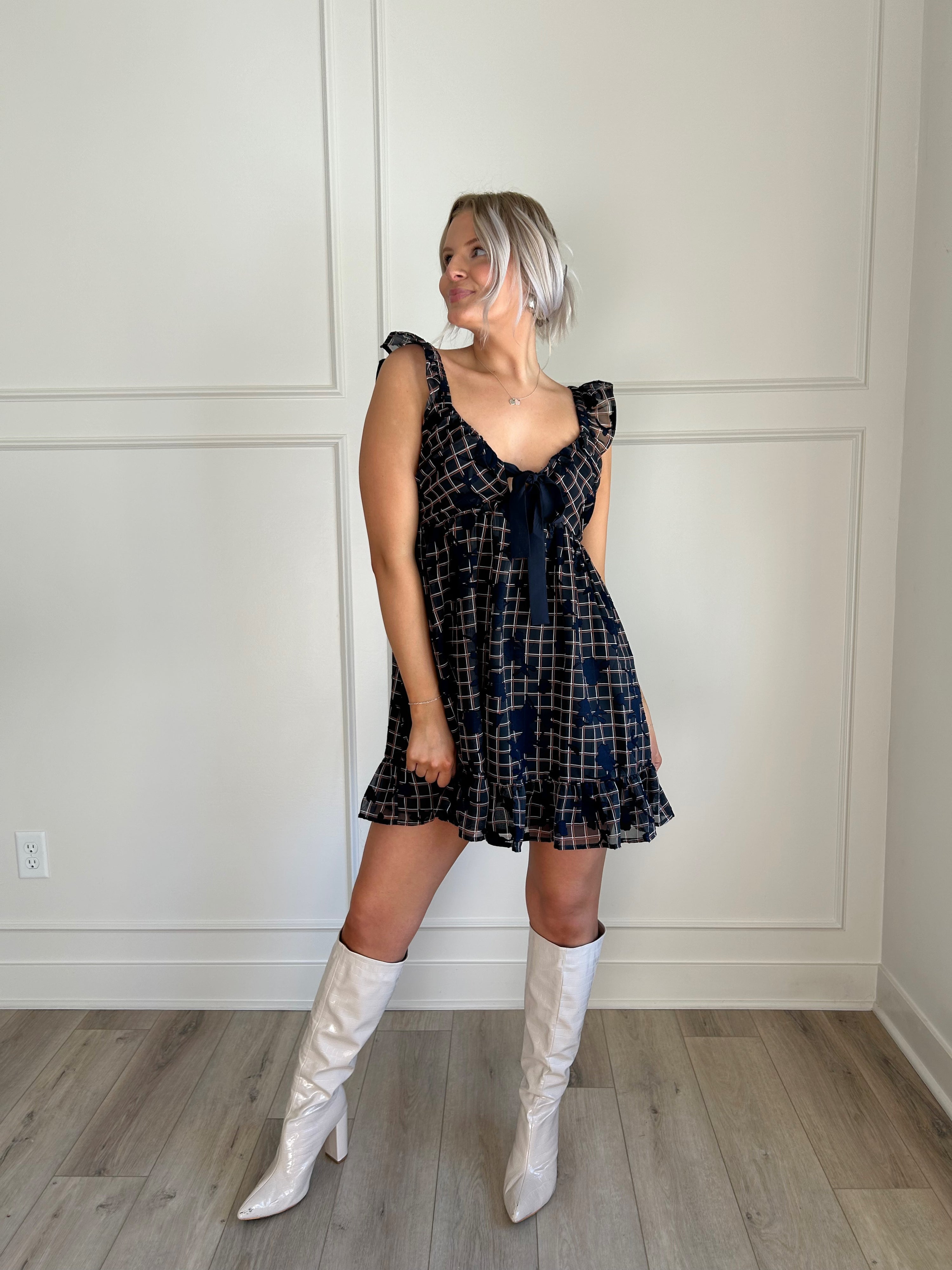 Navy plaid babydoll dress with ruffle sleeves, bow tie detail, and playful hemline.