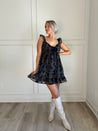 Navy plaid babydoll dress with ruffle sleeves, bow tie detail, and playful hemline.