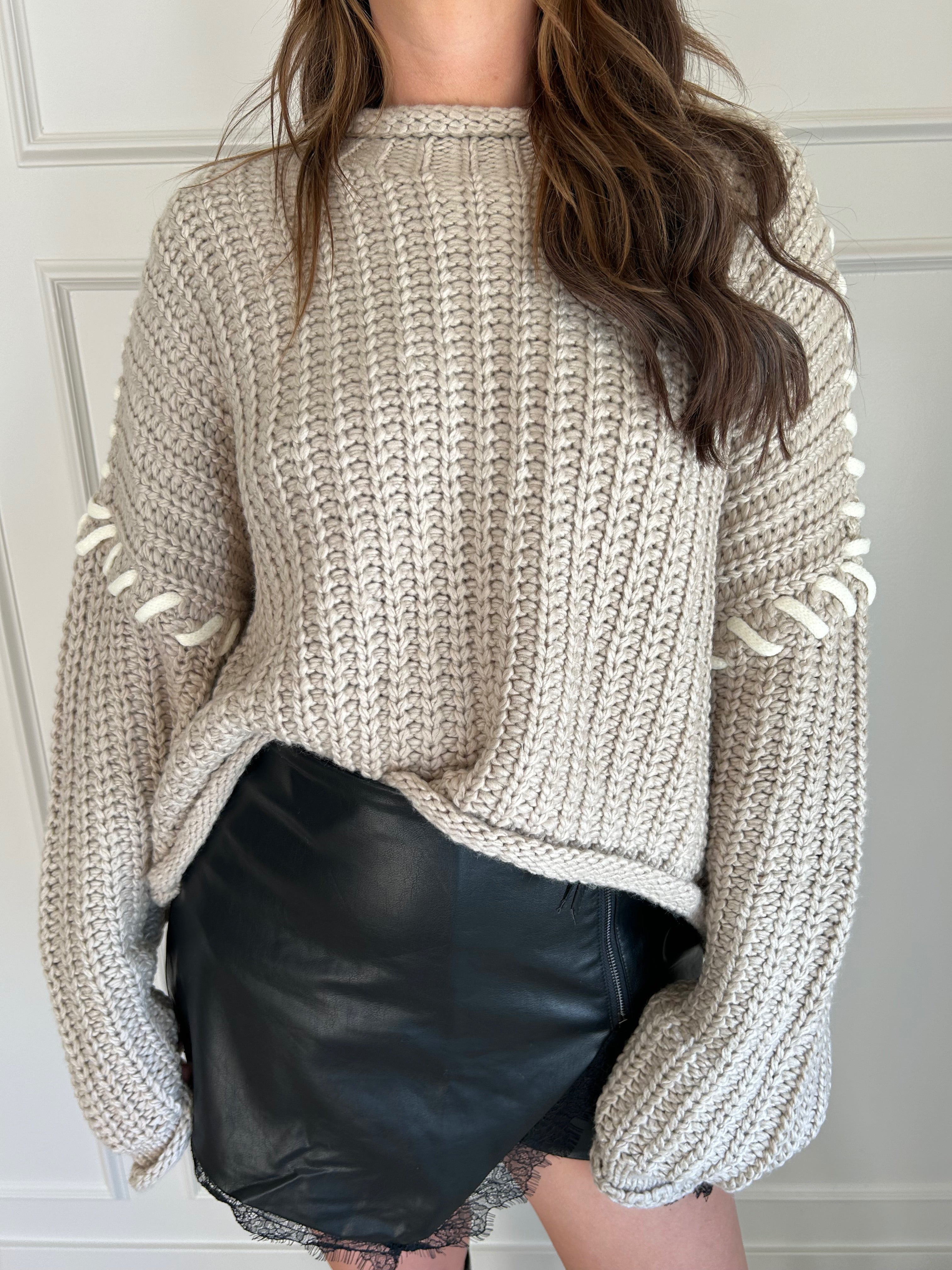 Beige chunky knit sweater with lace-up sleeve details and cozy fit.