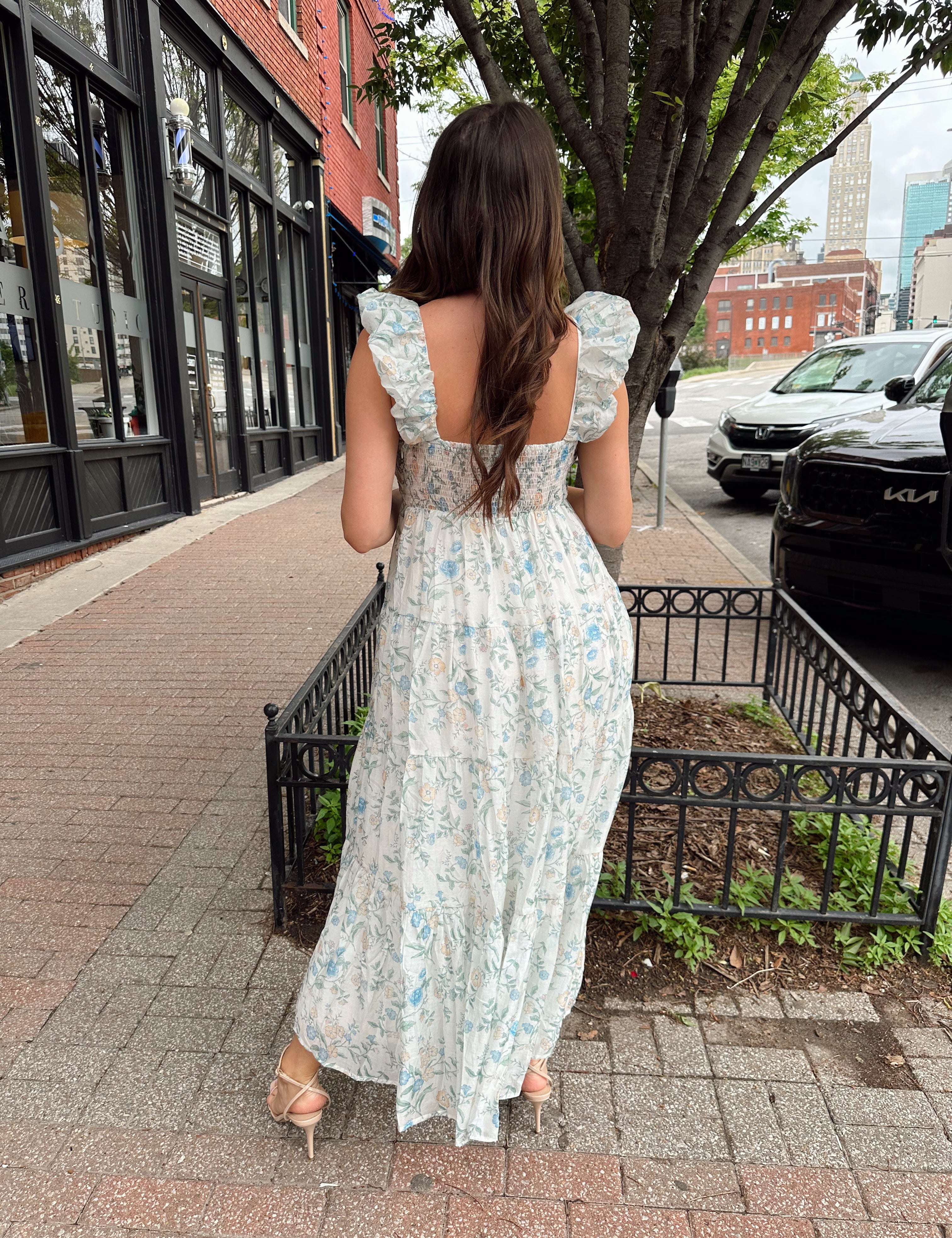 Woman in a blue floral maxi dress with ruffle straps, v-neck, and tiered skirt
