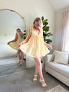 Woman wearing yellow embroidered mini dress with tie straps and floral detail
