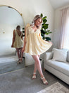 Woman wearing yellow embroidered mini dress with tie straps and floral detail