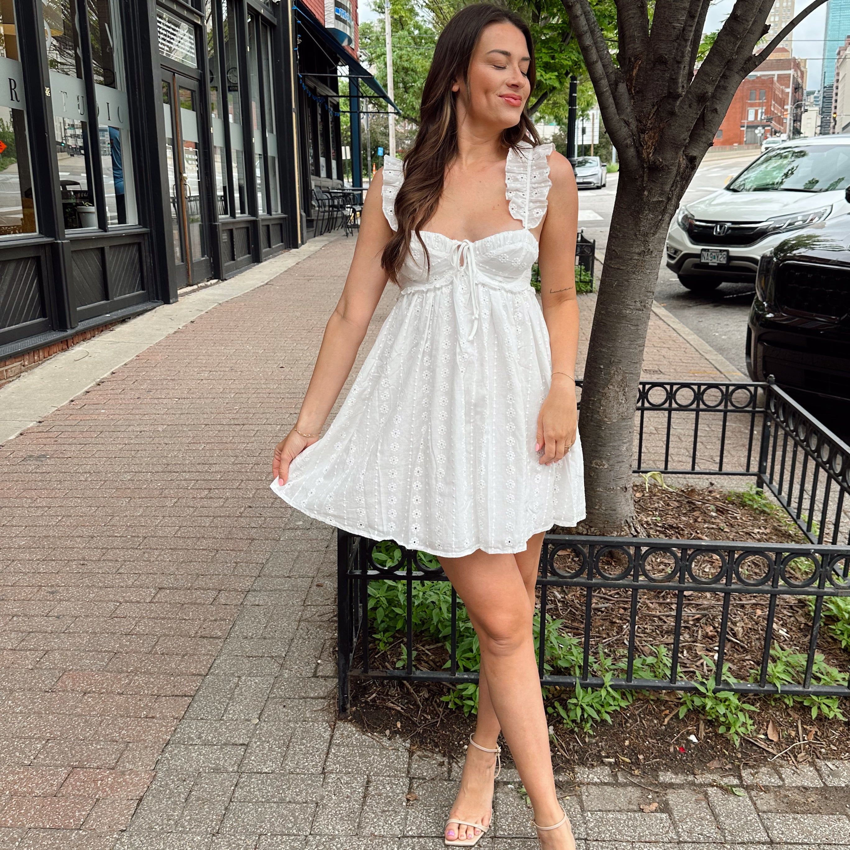 Woman in white eyelet mini dress with ruffle straps, tie front, and open back