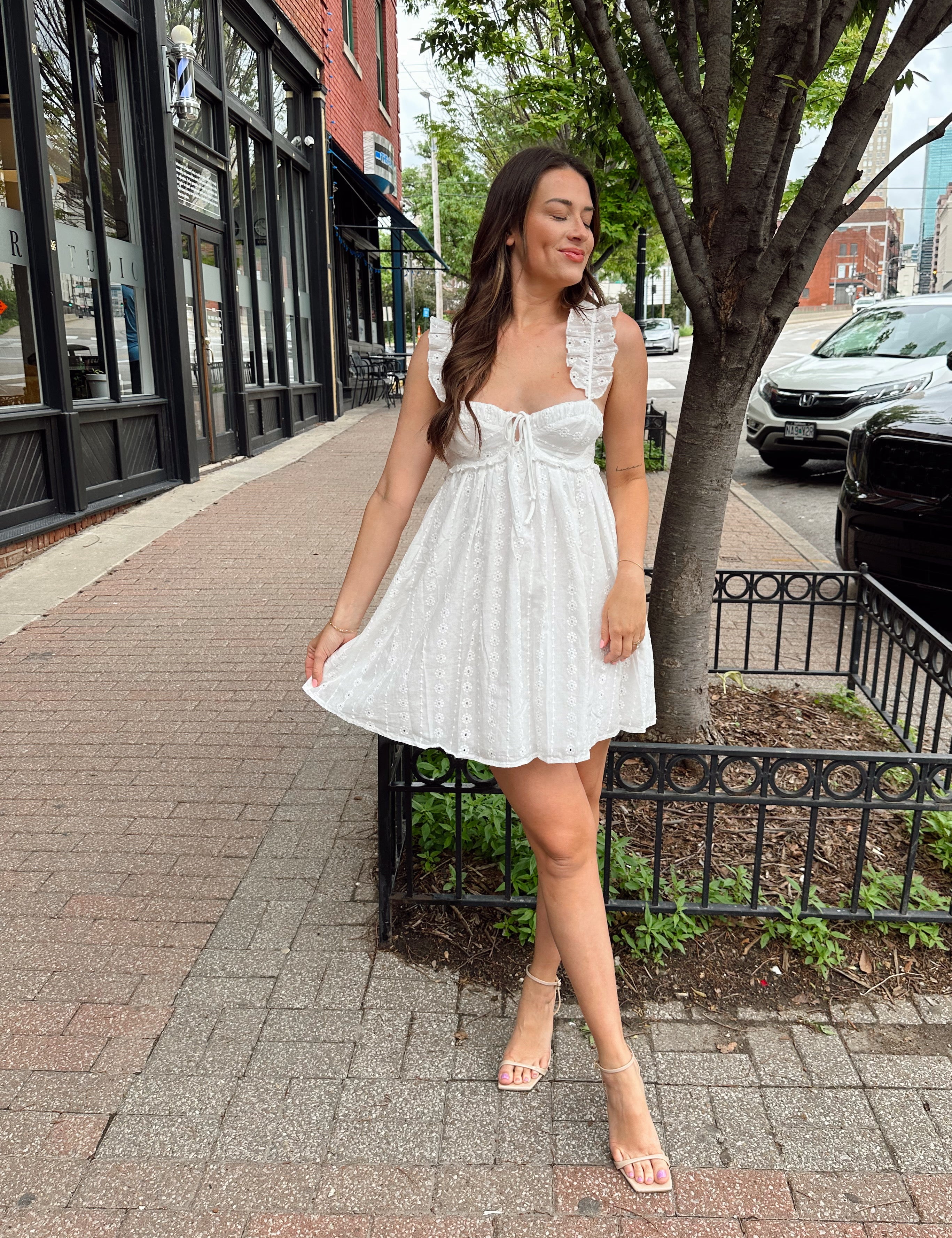 Woman in white eyelet mini dress with ruffle straps, tie front, and open back