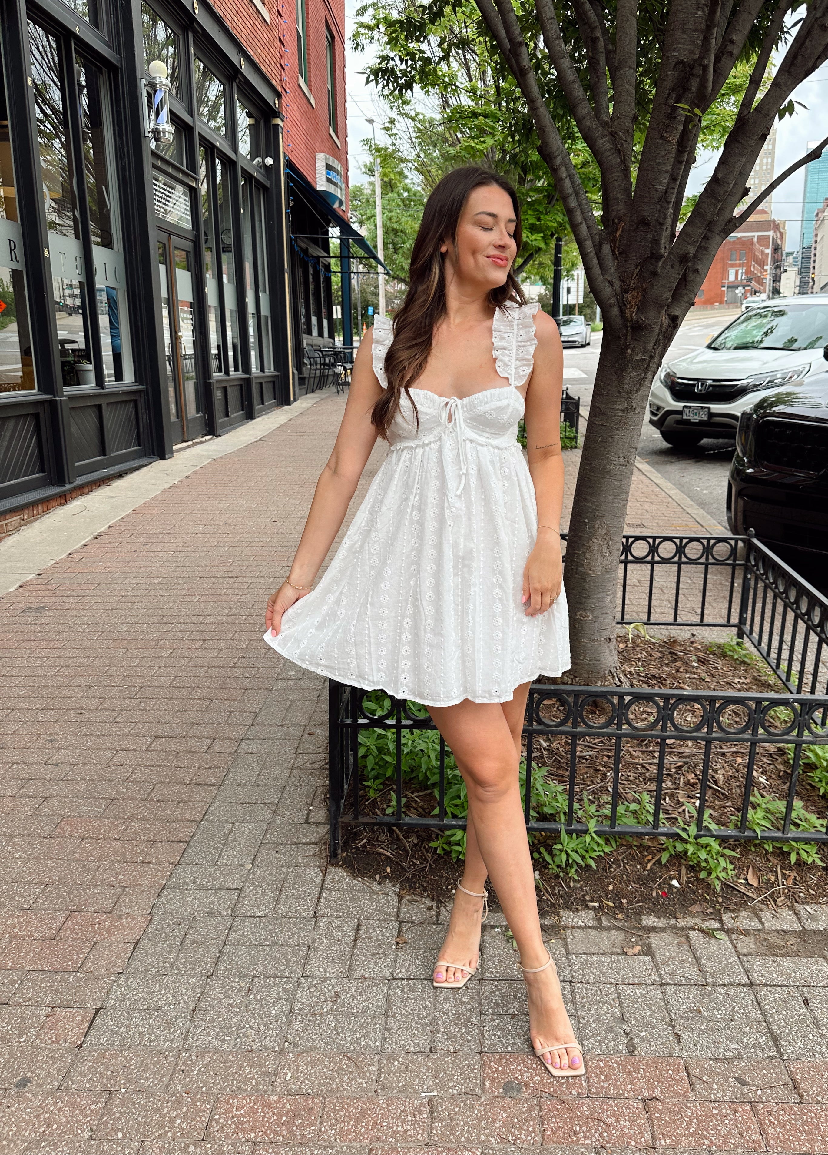 Woman in white eyelet mini dress with ruffle straps, tie front, and open back