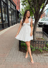 Woman in white eyelet mini dress with ruffle straps, tie front, and open back