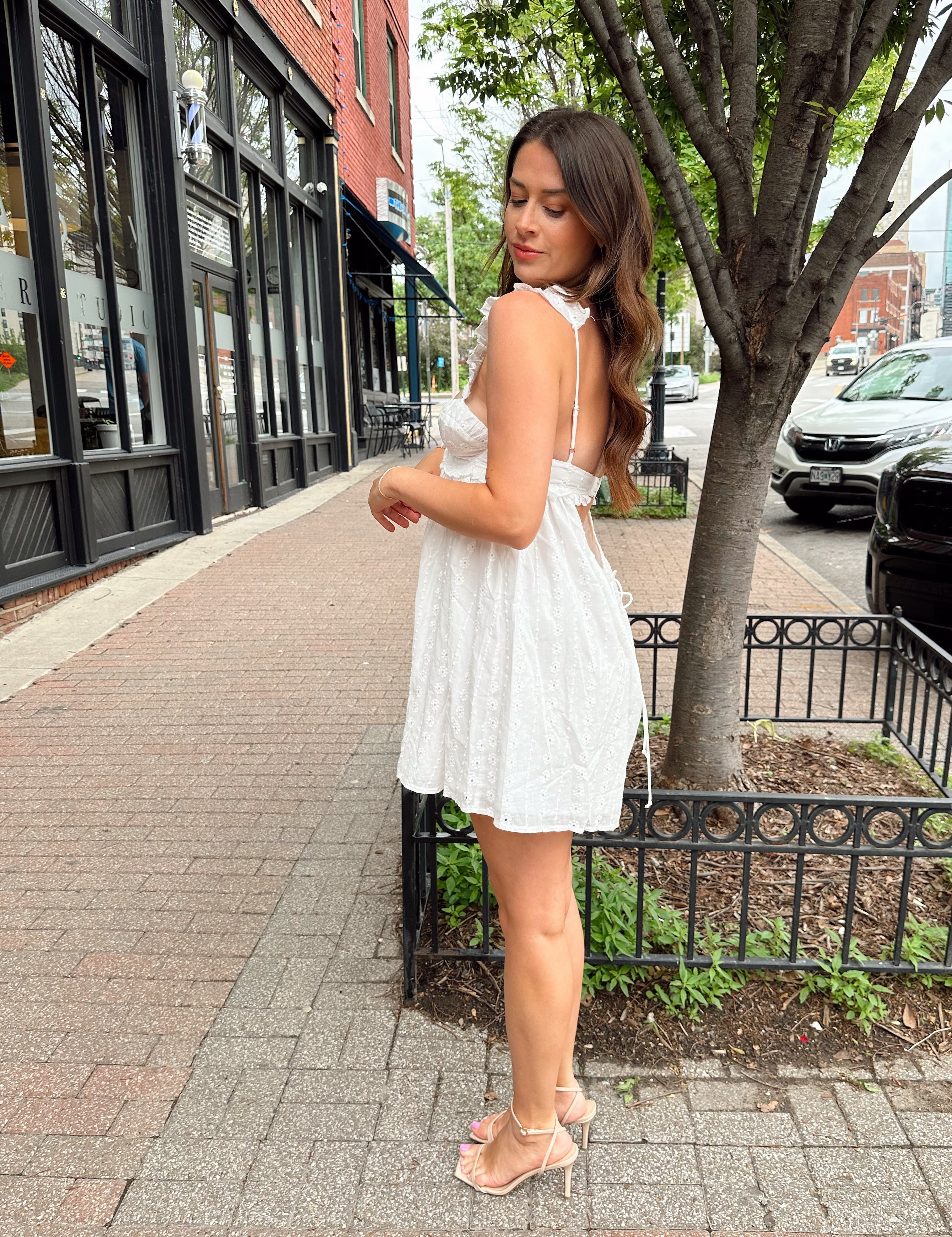 Woman in white eyelet mini dress with ruffle straps, tie front, and open back