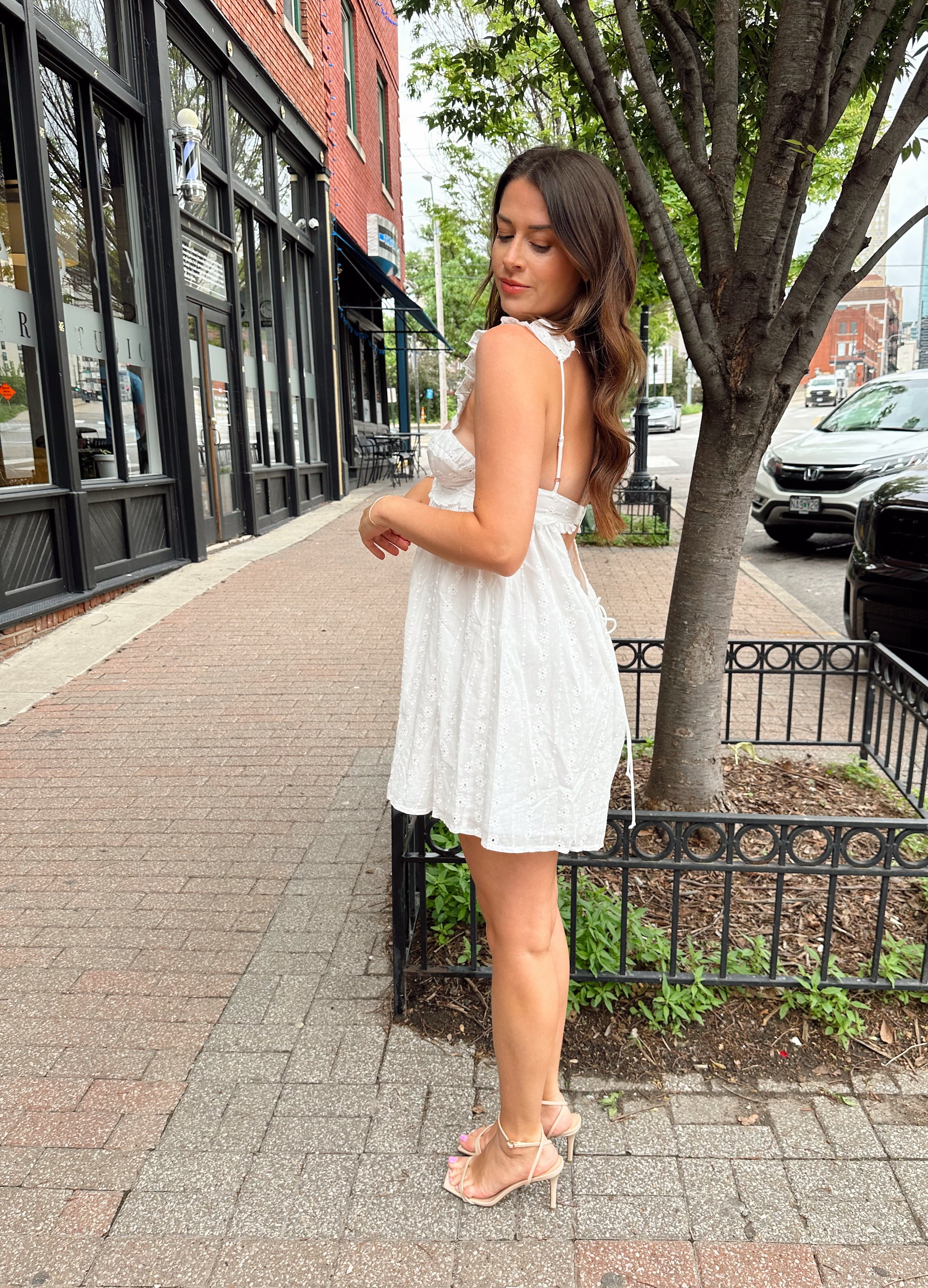 Woman in white eyelet mini dress with ruffle straps, tie front, and open back