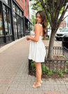 Woman in white eyelet mini dress with ruffle straps, tie front, and open back
