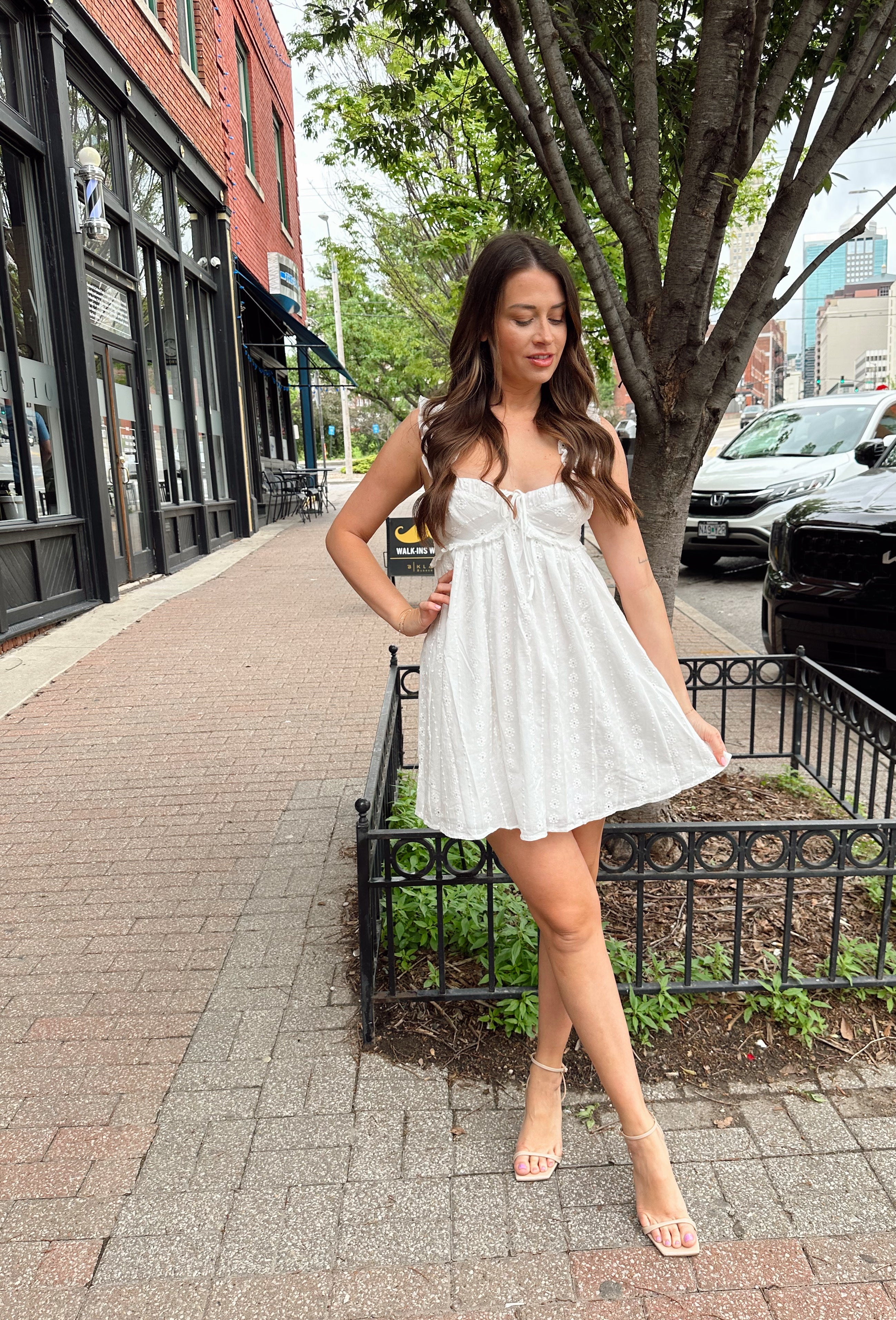 Woman in white eyelet mini dress with ruffle straps, tie front, and open back
