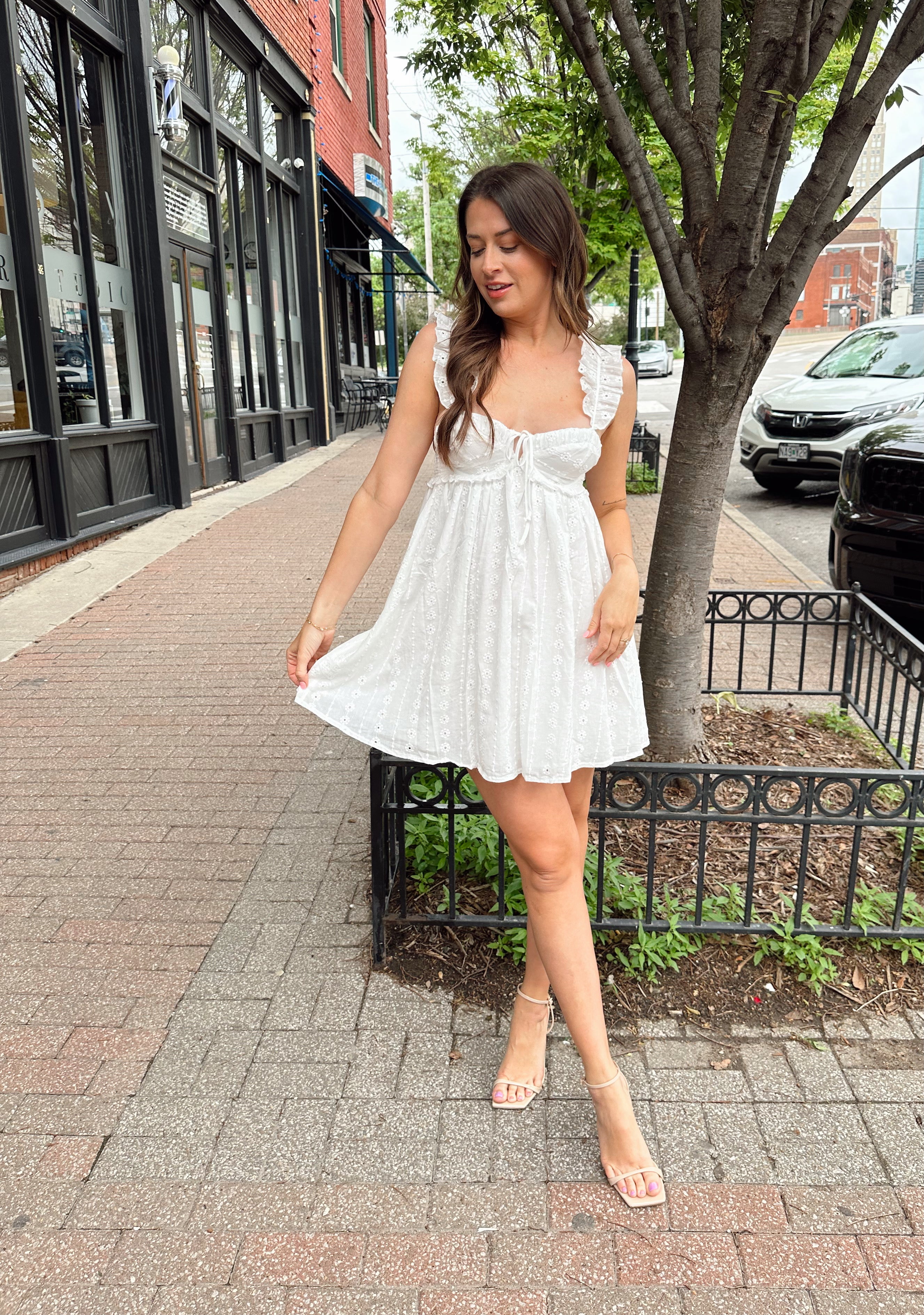 Woman in white eyelet mini dress with ruffle straps, tie front, and open back