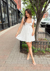 Woman in white eyelet mini dress with ruffle straps, tie front, and open back