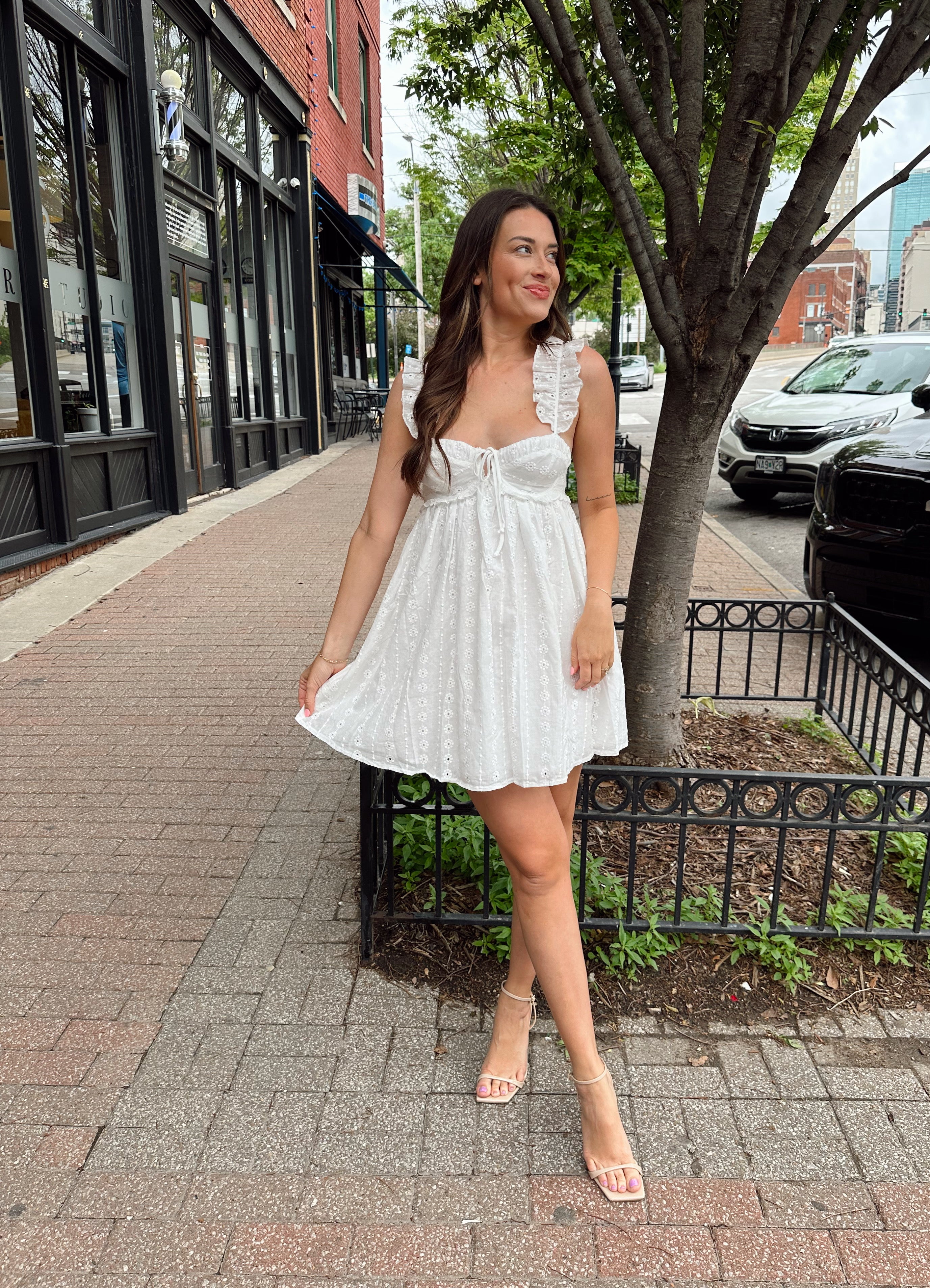 Woman in white eyelet mini dress with ruffle straps, tie front, and open back