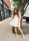 Woman in white eyelet mini dress with ruffle straps, tie front, and open back